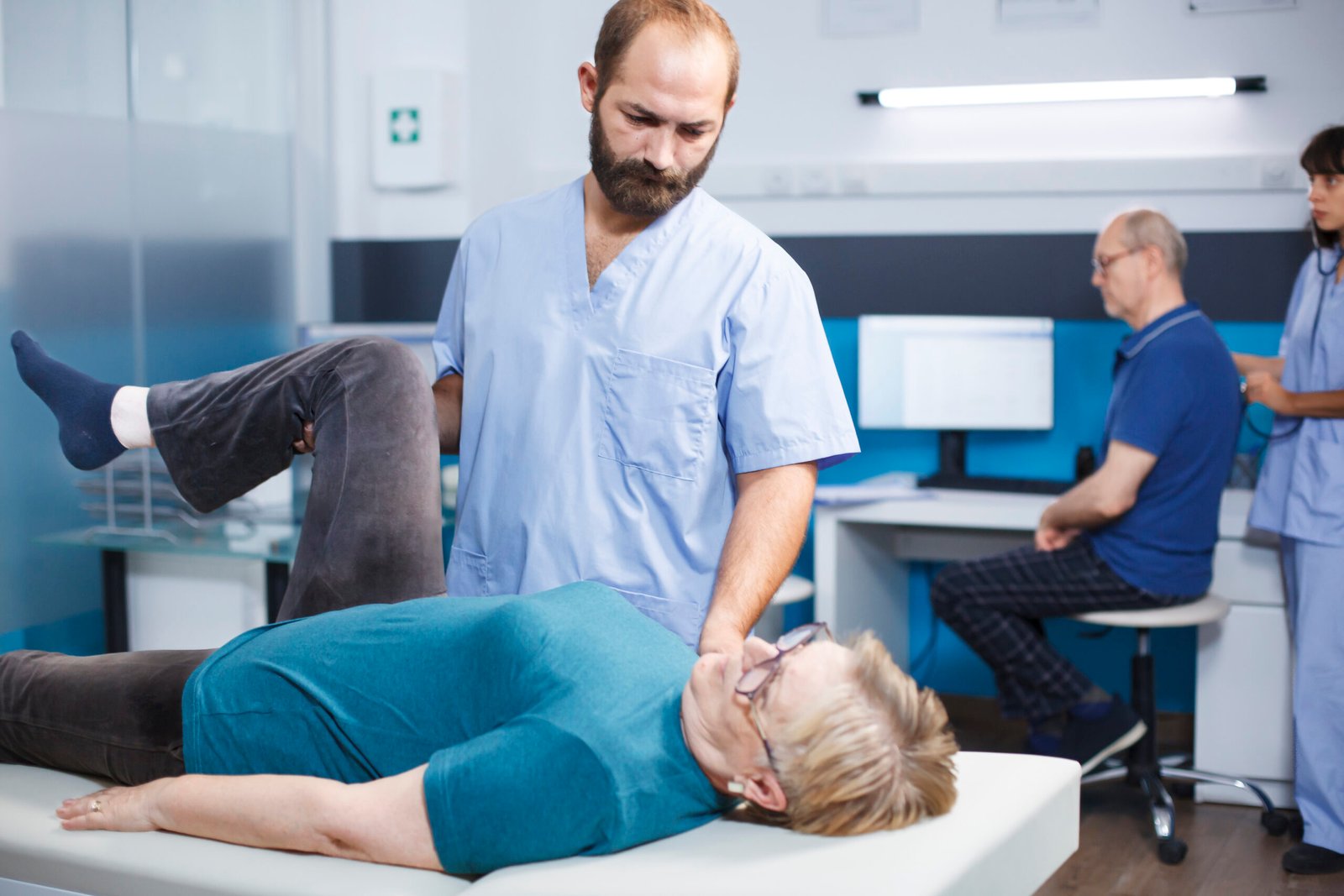 Physiotherapist helping aged woman with leg muscle pain in osteopathy clinic. Chiropractor assistant treating patient with knee injury for physical recovery, giving support.